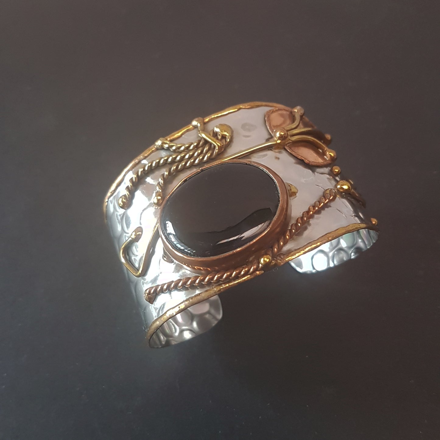 Silver cuff bracelet with a large oval shaped black onyx stone. Unique mixed metal design with copper, brass and silver. Flexible adjustable size.