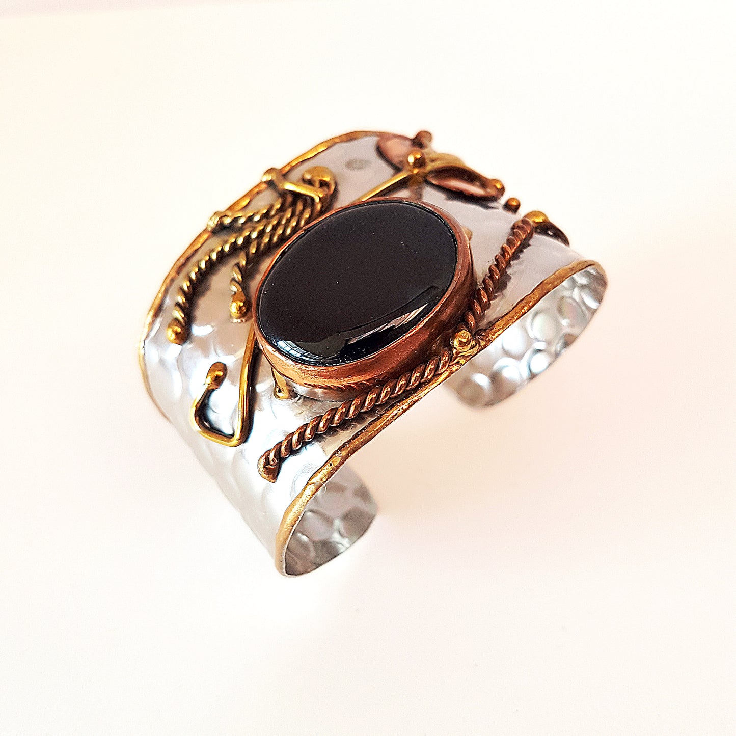 Silver cuff bracelet with a large oval shaped black onyx stone. Unique mixed metal design with copper, brass and silver. Flexible adjustable size.