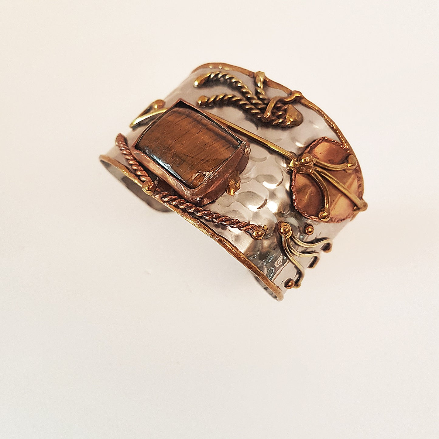 Silver cuff bracelet with rectangle shape tigereye stone. Adjustable fit. Mixed metal artisan design with copper & brass detail.