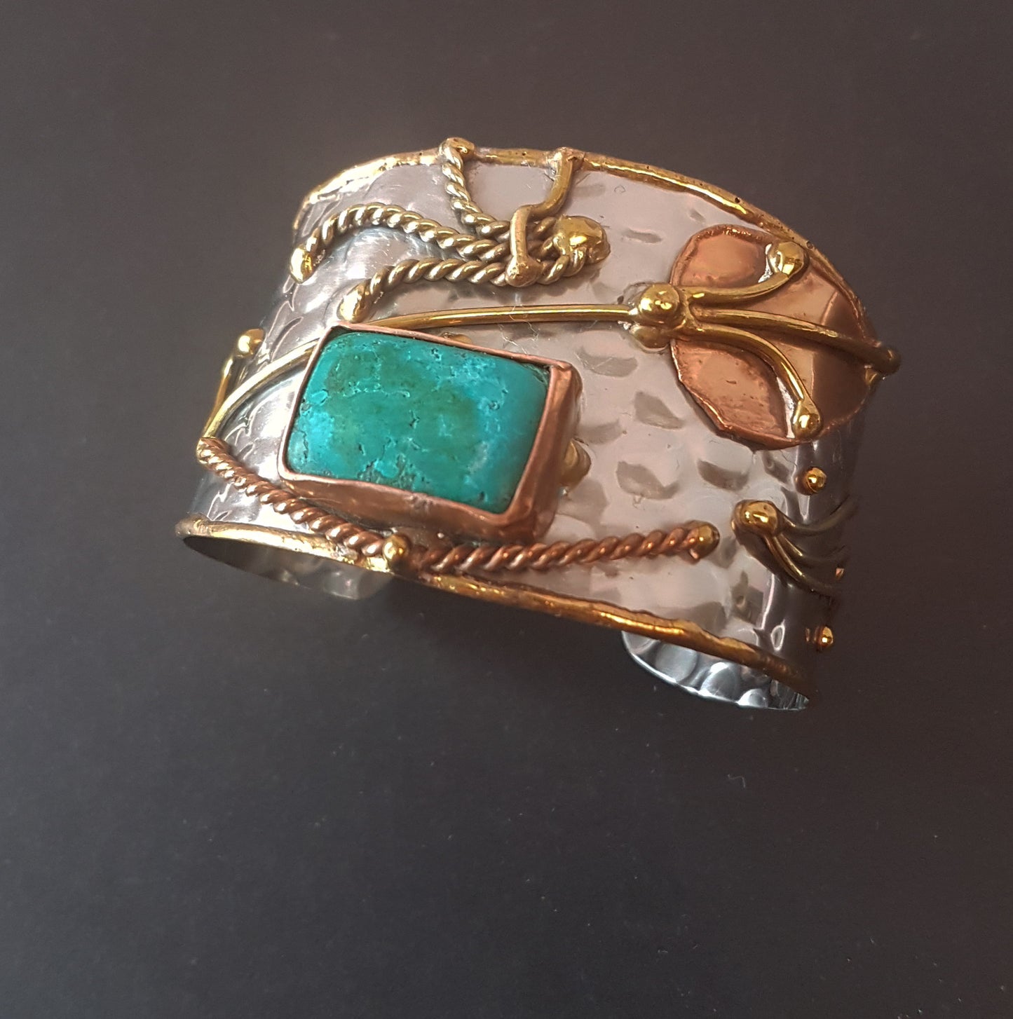 Silver cuff bracelet with an inlaid turquoise stone. Hammered trimetal design with copper & brass detail.
