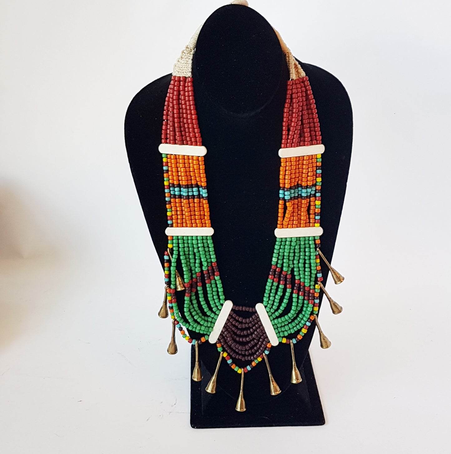 Collier de perles tribal dans une superbe combinaison d'orange, de marron, de vert et de rouille. Fermeture par bouton en os. Détail de corne en métal bronze antique.