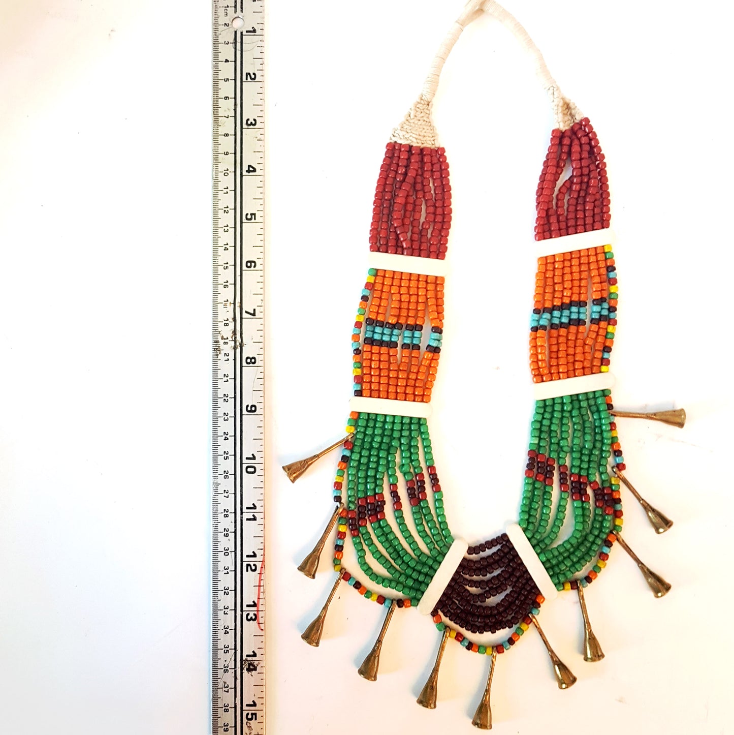 Collier de perles tribal dans une superbe combinaison d'orange, de marron, de vert et de rouille. Fermeture par bouton en os. Détail de corne en métal bronze antique.