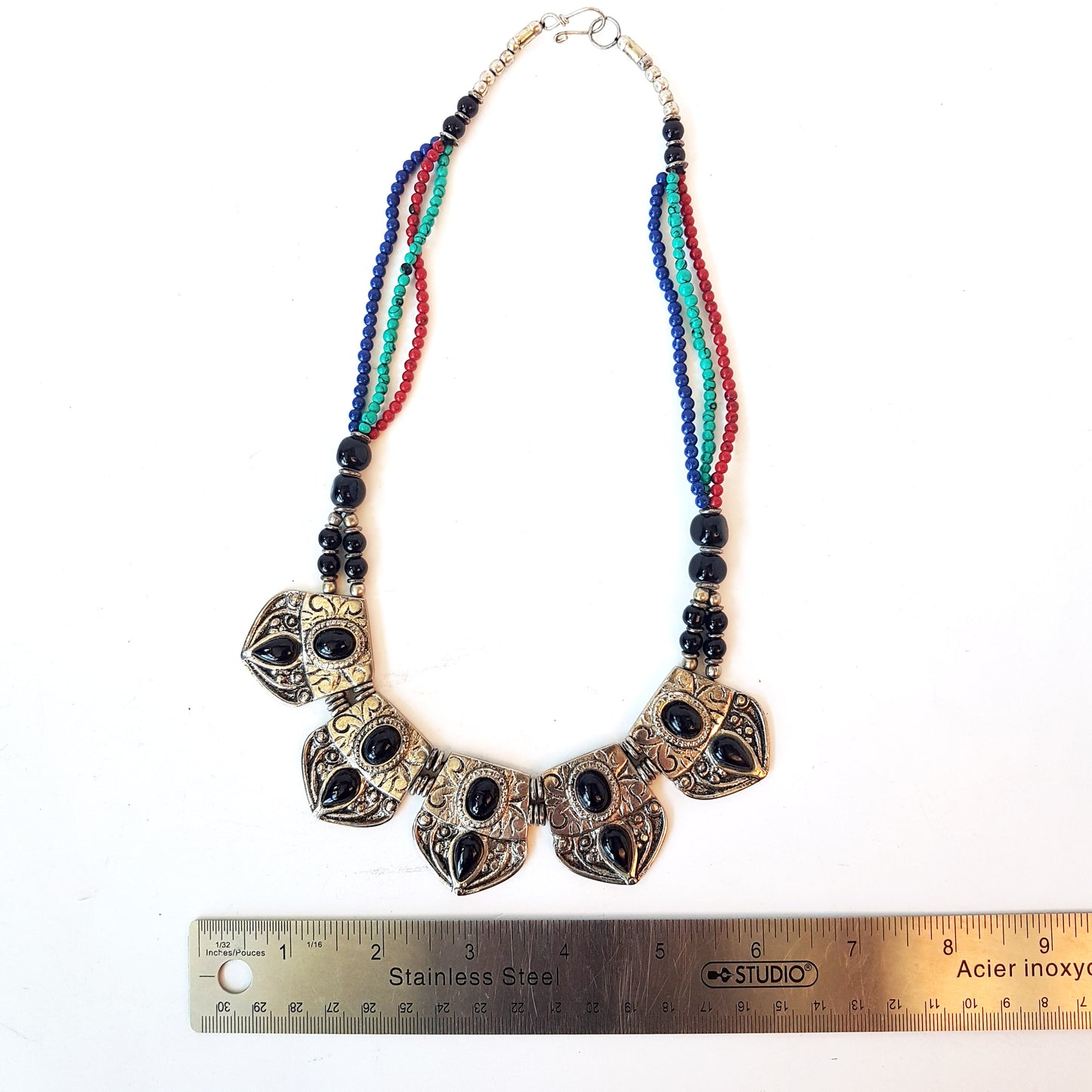 Collier indo-tibétain dramatique avec des pierres d'onyx noires incrustées sur du métal argenté gaufré. Finition corde perlée multicolore.
