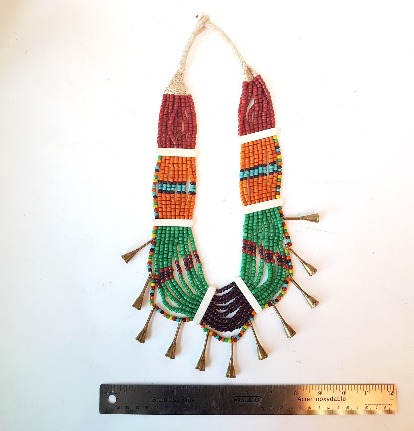 Collier de perles tribal dans une superbe combinaison d'orange, de marron, de vert et de rouille. Fermeture par bouton en os. Détail de corne en métal bronze antique.