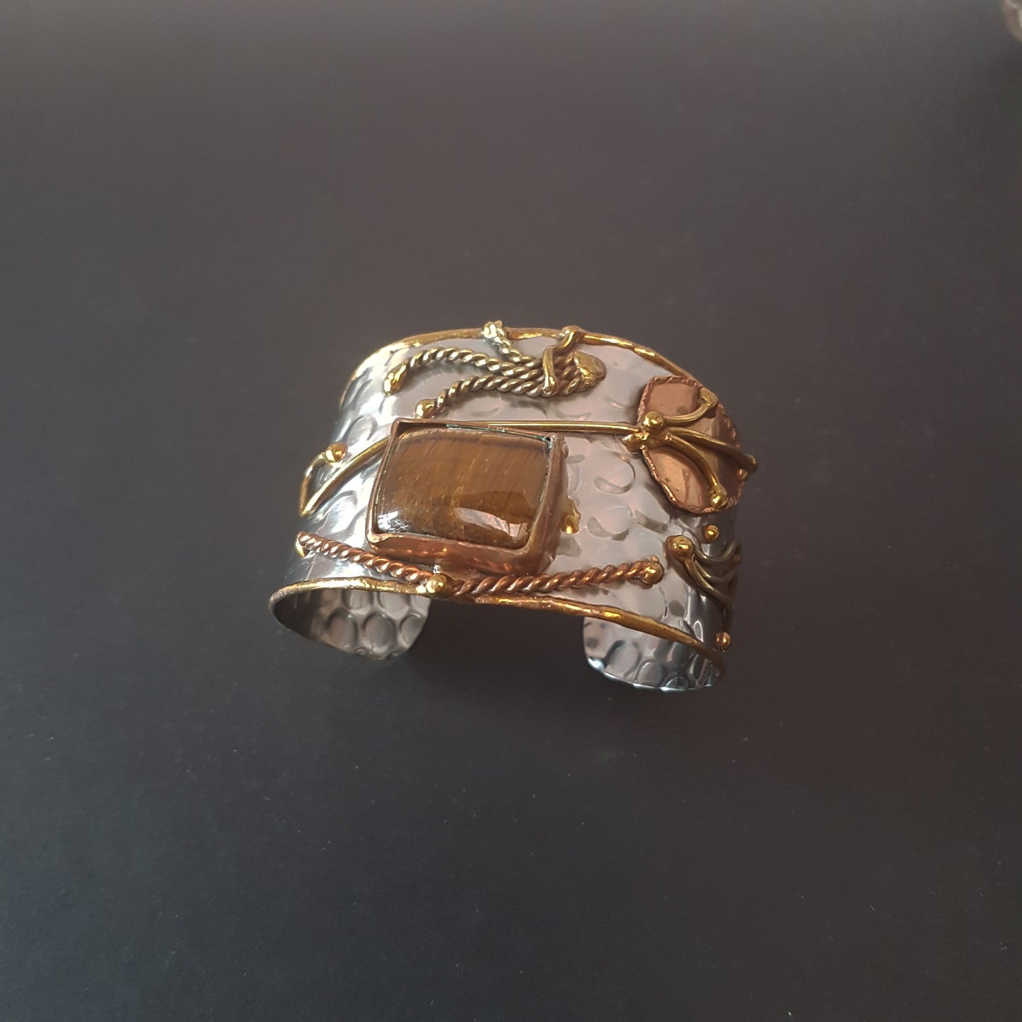 Bracelet manchette en argent avec pierre oeil de tigre de forme rectangle. Ajustement réglable. Conception artisanale en métal mélangé avec des détails en cuivre et en laiton.