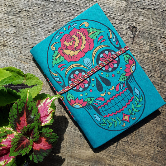 Teal blue skull sketchbook jotter 5 by 7 inches with blank artisan paper pages. Colorful gothic day of the dead sugarskull design diary in teal.