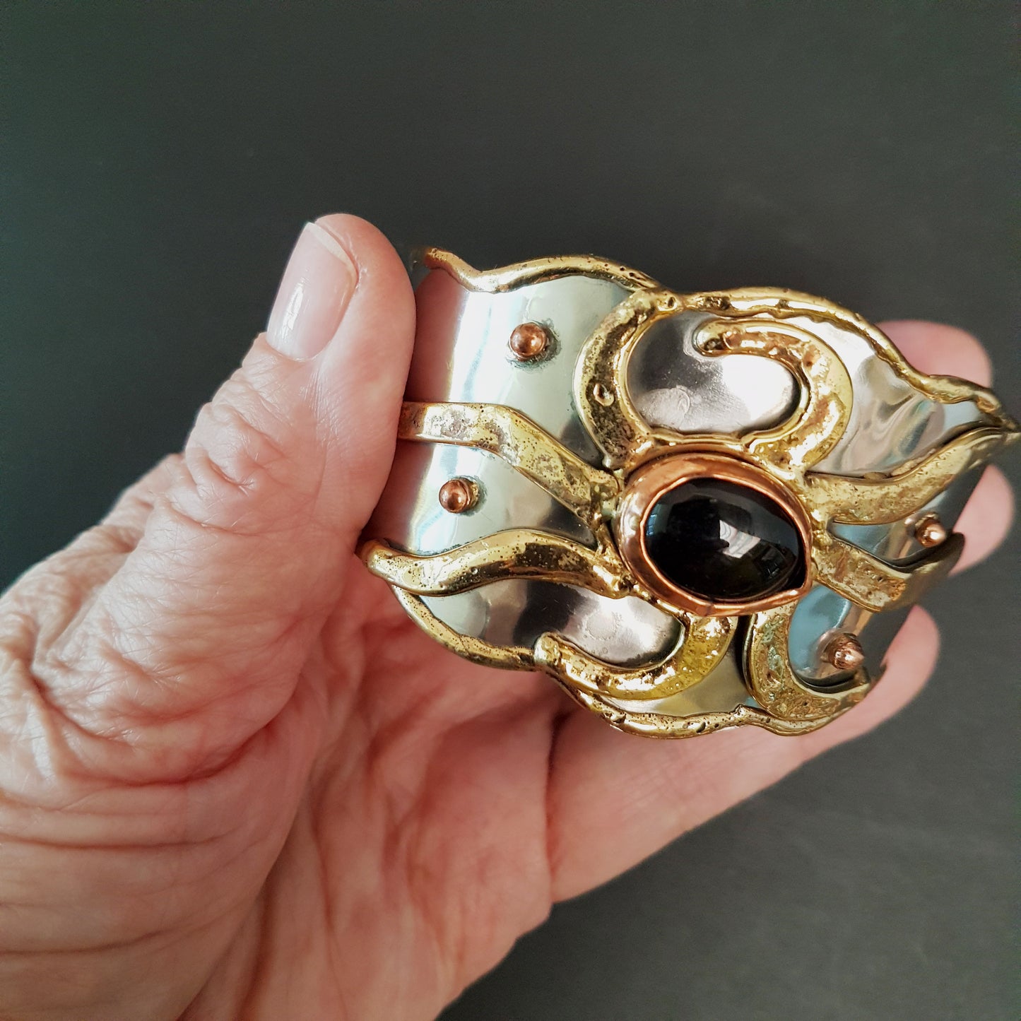 Silver cuff bracelet with inlaid gemstone center. Medieval Celtic sunrise design with brass detail. Vintage handwrought artisan metalwork.